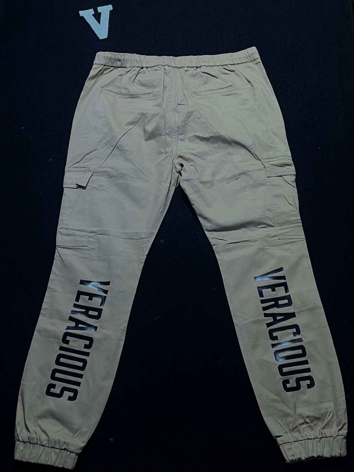 Beige cargo pants with 'VERACIOUS' branding on a black background